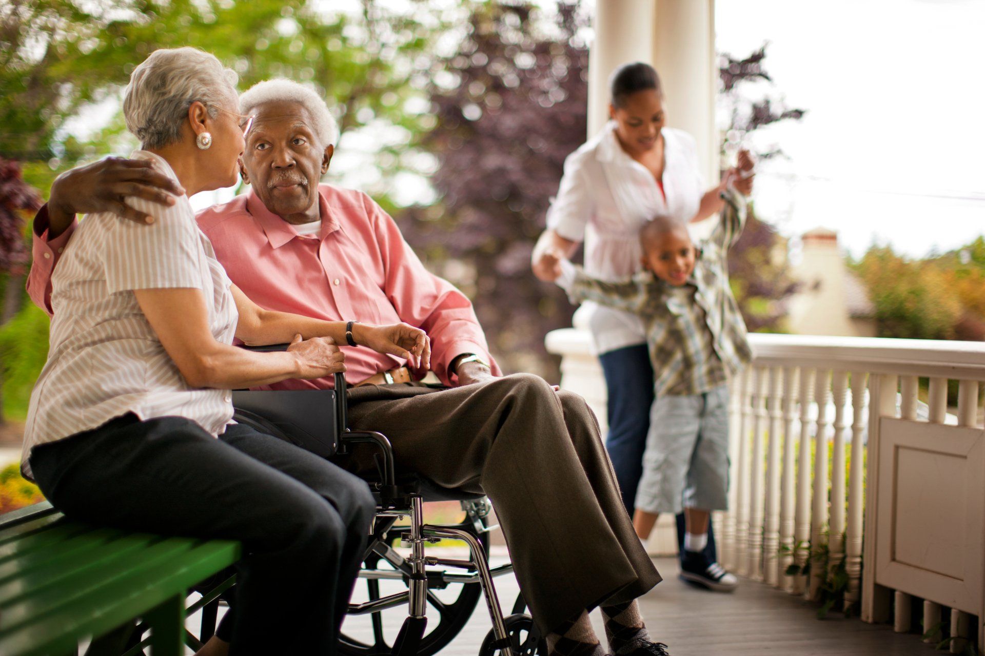 A man in a wheelchair is sitting on a porch with a woman and a child.