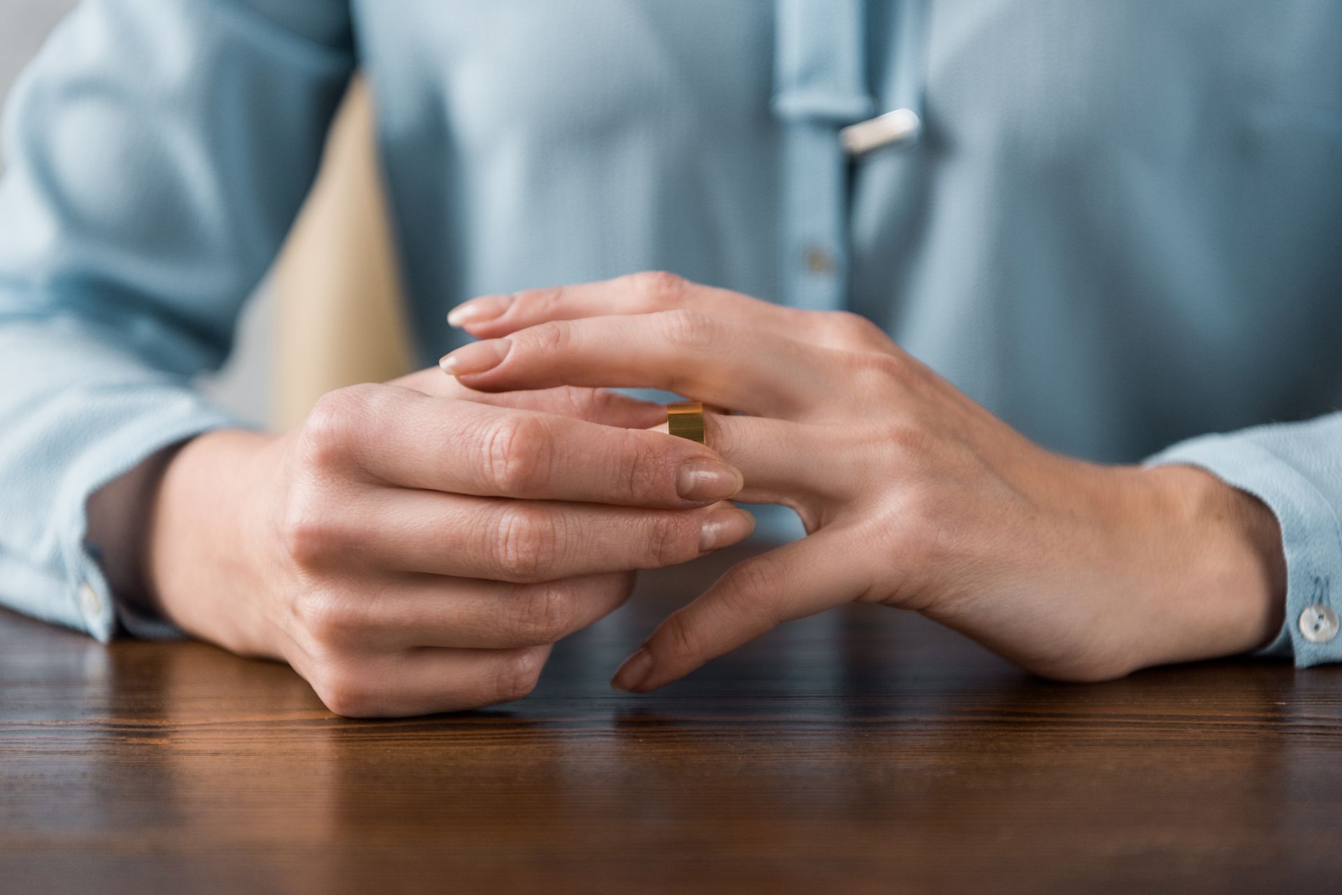 A woman is sitting at a table holding a wedding ring in her hands.