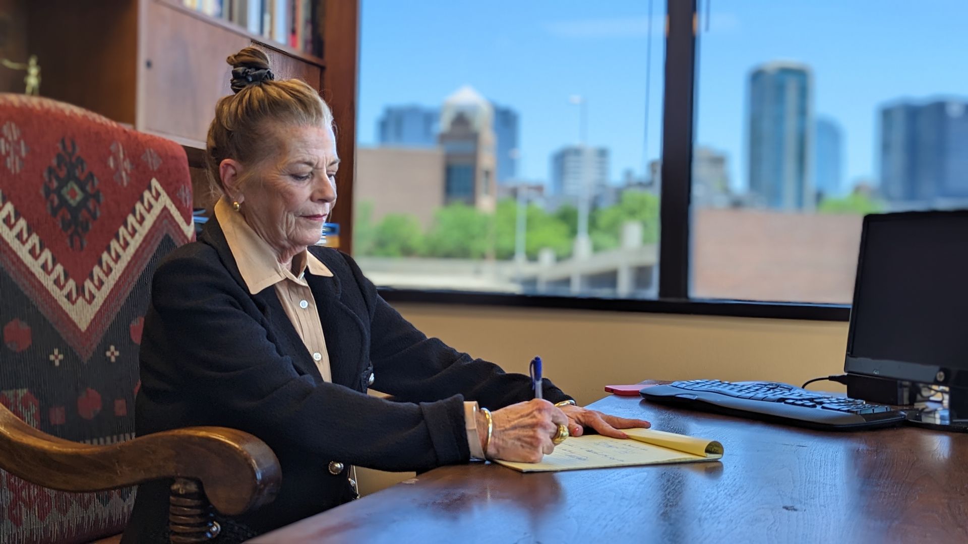 A woman is sitting at a desk writing on a piece of paper.