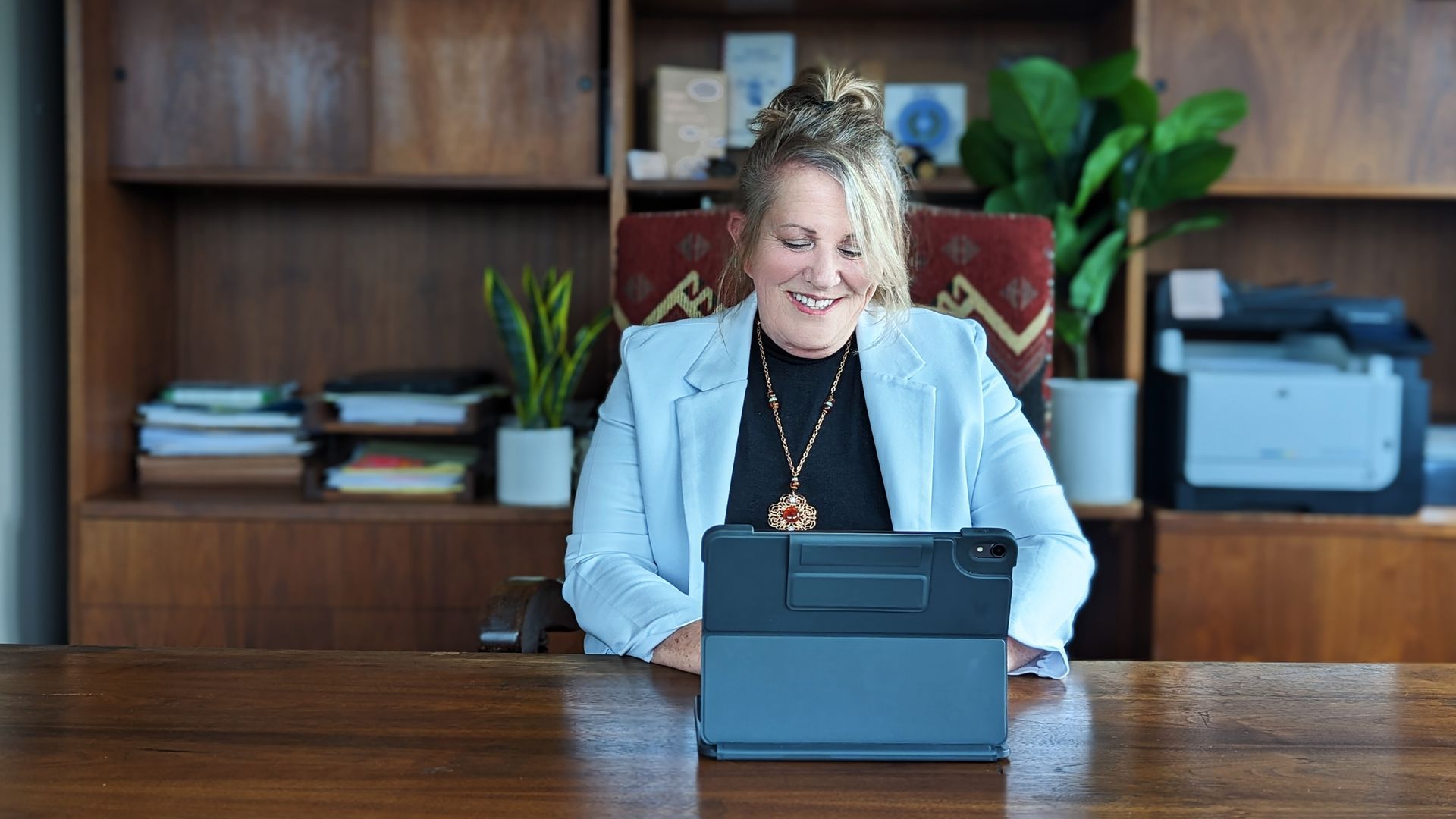 A woman is sitting at a desk using a tablet computer.