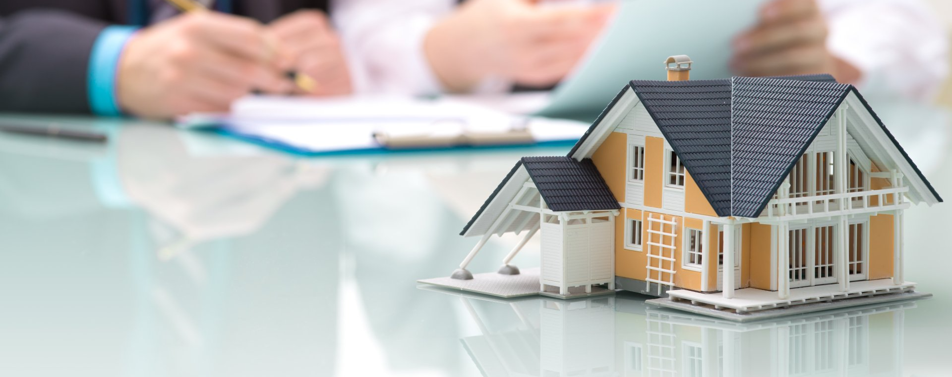 A model house is sitting on a table next to a person signing a document.