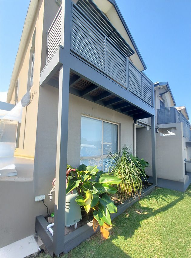 A House with a Balcony and Plants in Front of It — JWP Painting & Property Services in Ettalong Beach, NSW