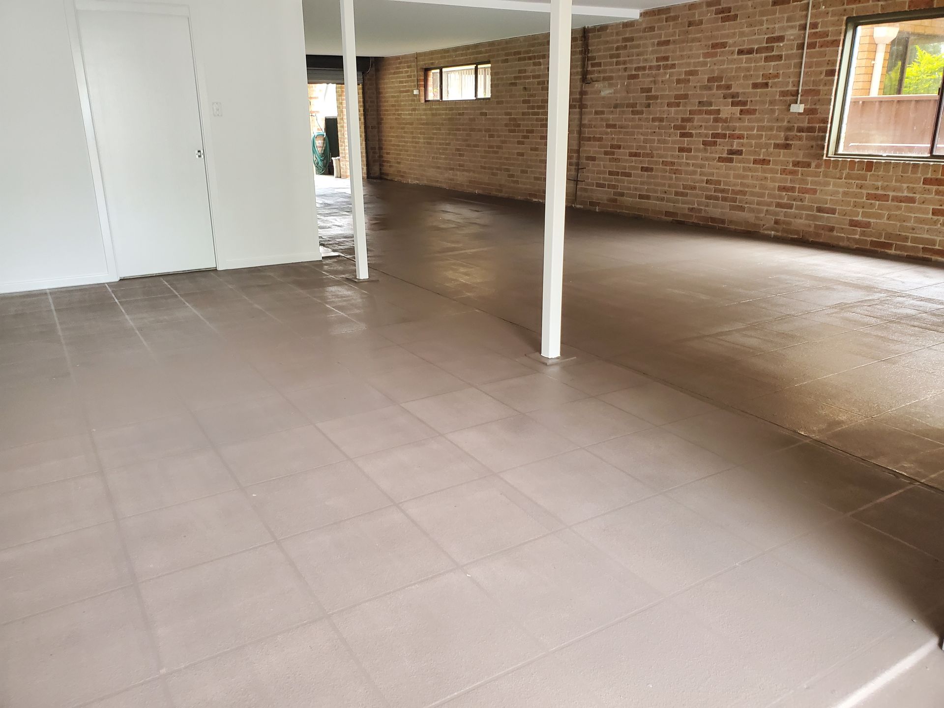 A Large Empty Room With a Tiled Floor and a Brick Wall — JWP Painting & Property Services in Ettalong Beach, NSW