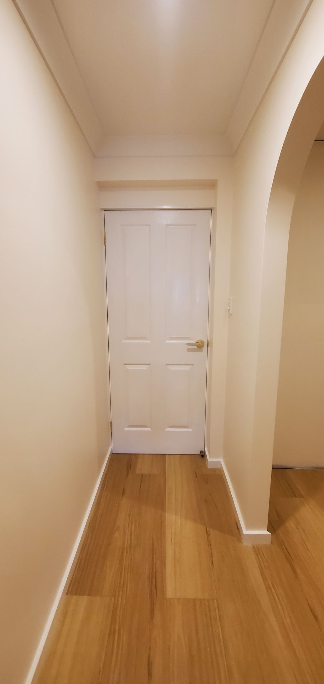 An Empty Hallway With Hardwood Floors and a White Door — JWP Painting & Property Services in Ettalong Beach, NSW