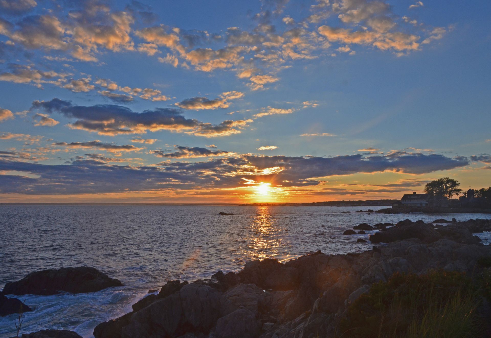 A sunset over a body of water with rocks in the foreground.