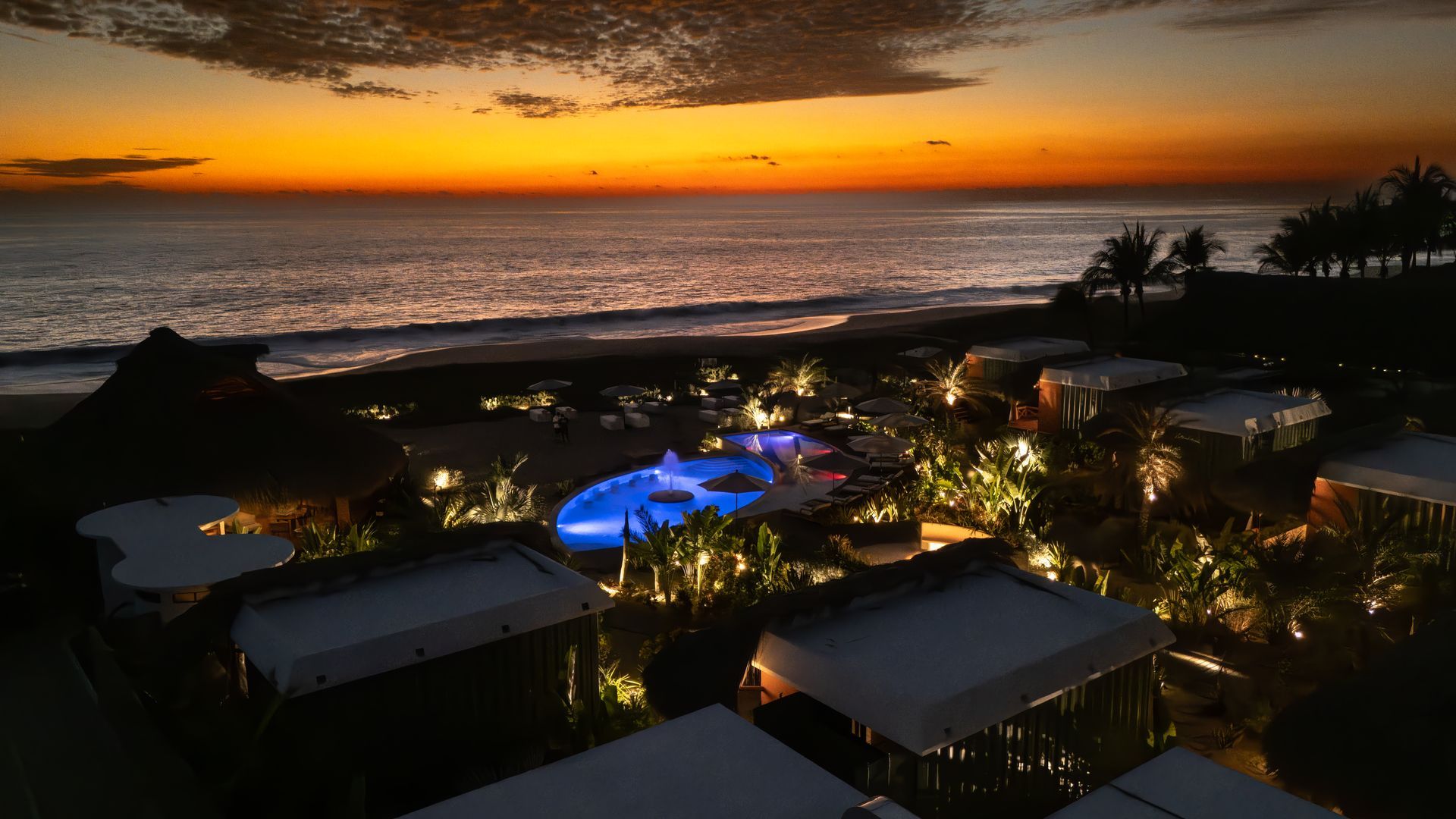 Una vista aérea de un complejo turístico al atardecer con una piscina en primer plano.