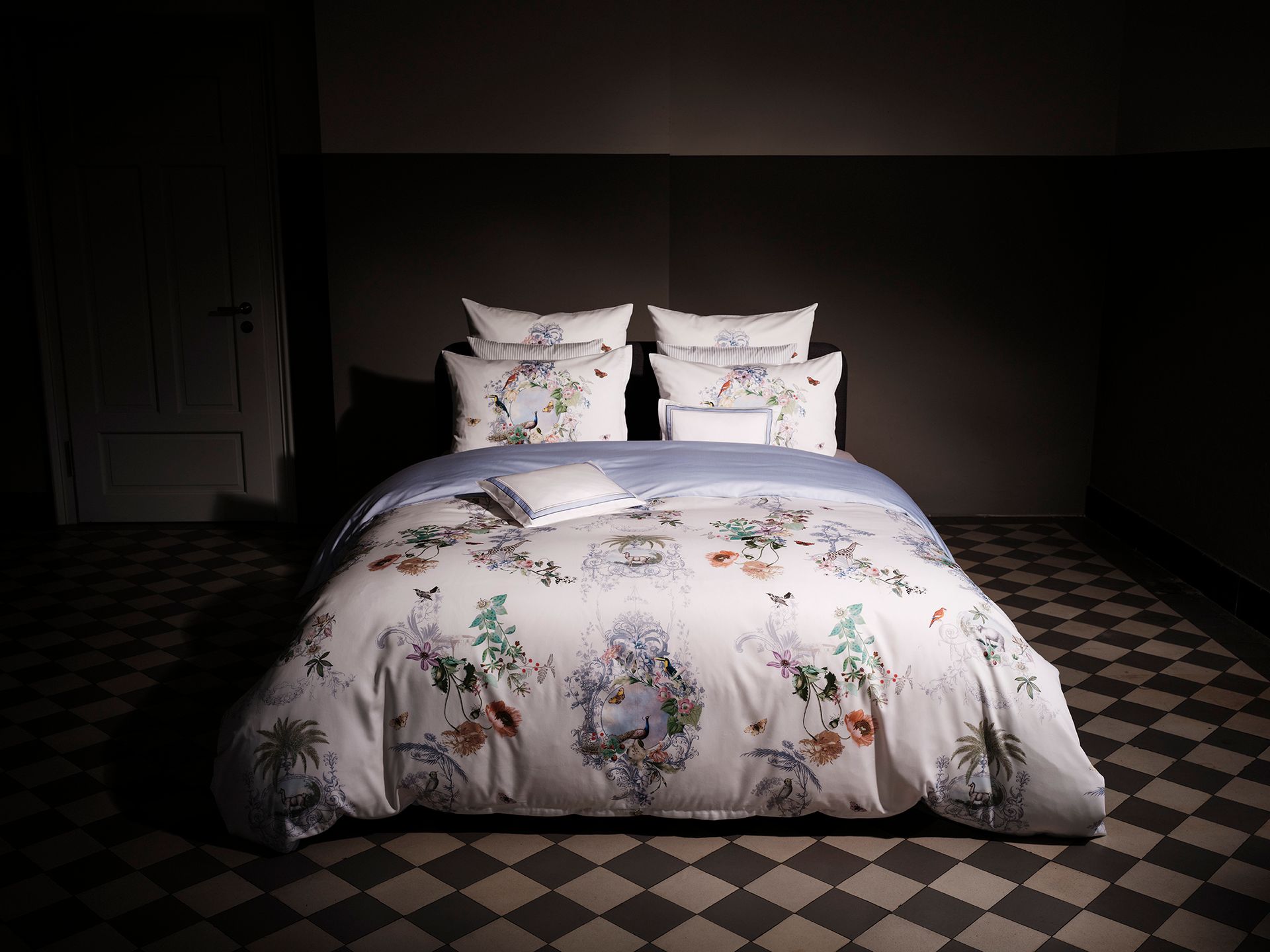 Bedroom with a floral duvet and pillows on a bed in a dimly lit room.