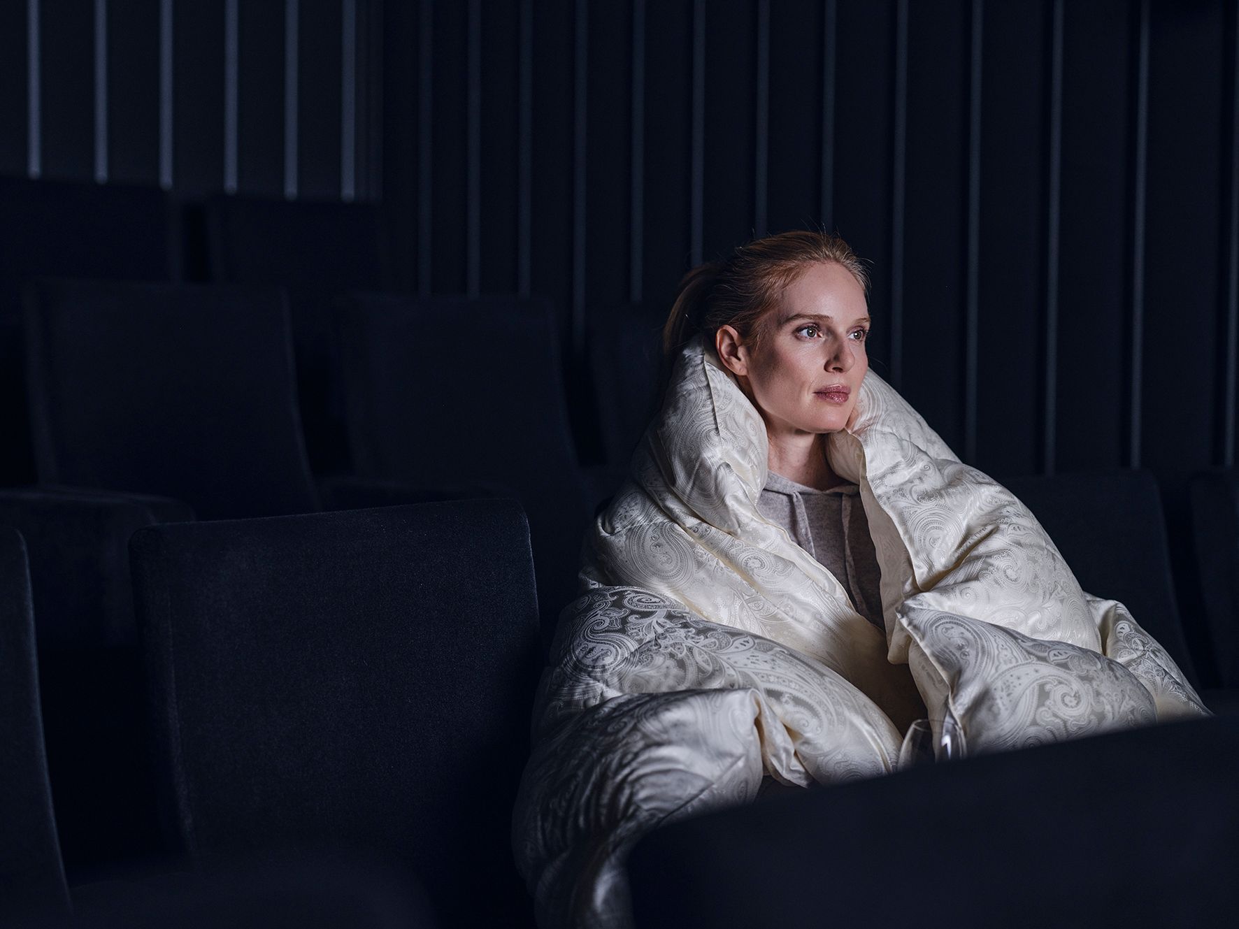 Woman wrapped in a white blanket sitting on a dark couch in a dimly lit room