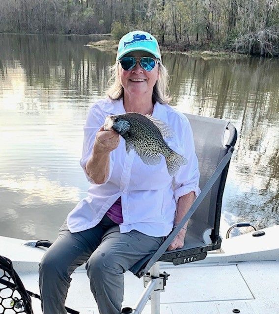 Woman seated in a kayak holds up a fish on a calm river