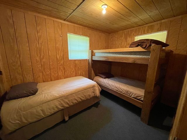 Small wooden cabin bedroom with a twin bed and a bunk bed under a slanted ceiling.