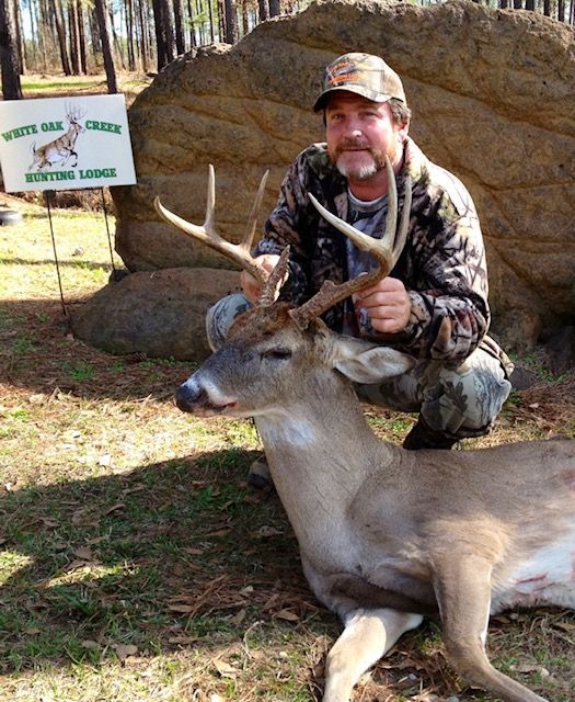 Hunter kneeling beside a deer he has just shot in a wooded area, holding the antlers.