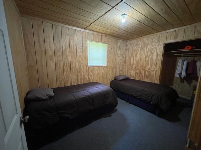 Small wood-paneled bedroom with two beds, a window, and an open closet.