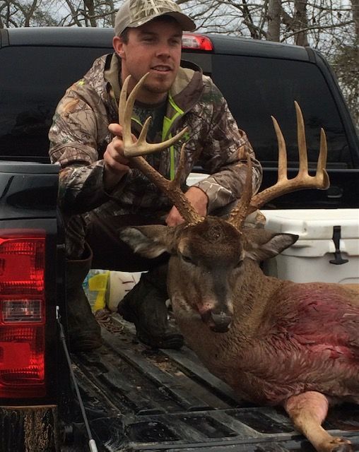 Hunter posing with a large deer in the bed of a pickup truck.