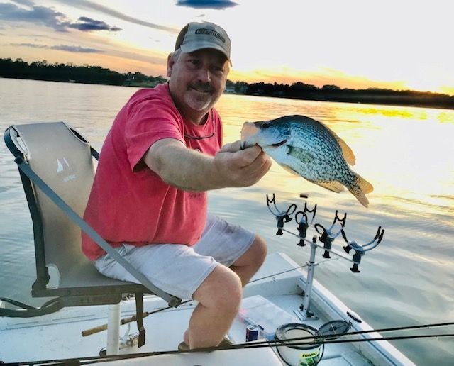 Man on a boat at sunset holding up a fish over calm water