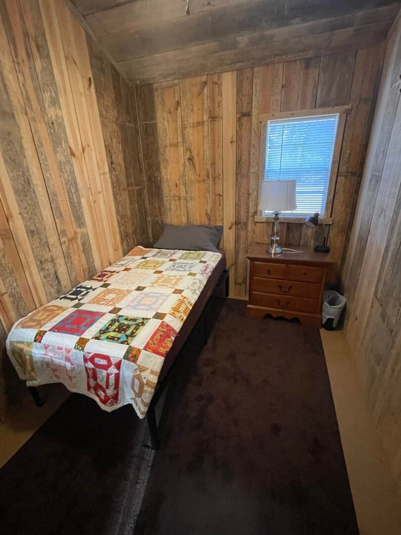 Small rustic bedroom with a twin bed, quilt, wooden dresser, and window.