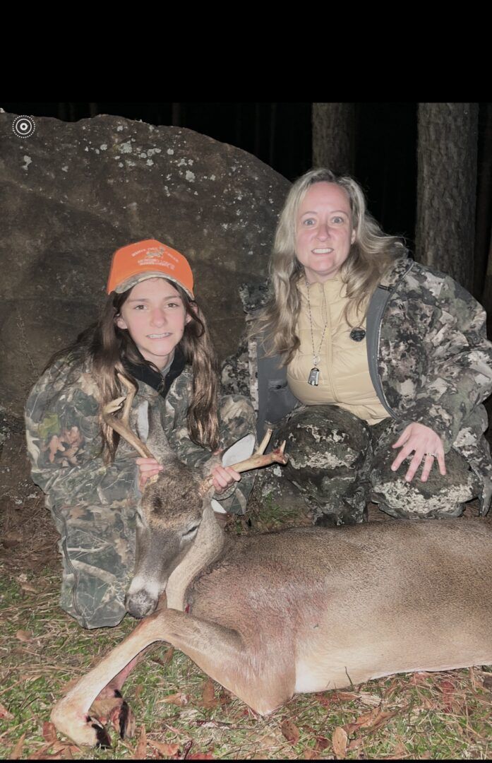 Two hunters in camouflage kneel beside a deer at night in the woods