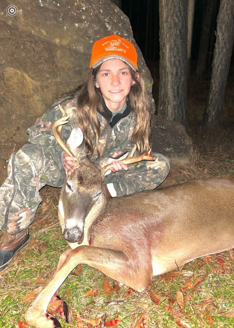 Hunter kneeling with a deer in the woods at dusk
