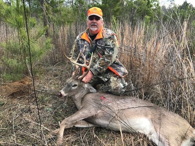 Hunter kneeling over a deer in a wooded area, holding its antlers.