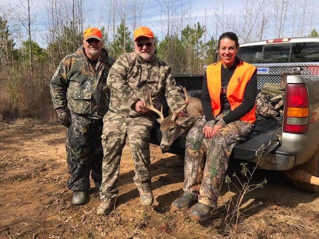 Three hunters posing with a deer beside a pickup truck in a wooded field