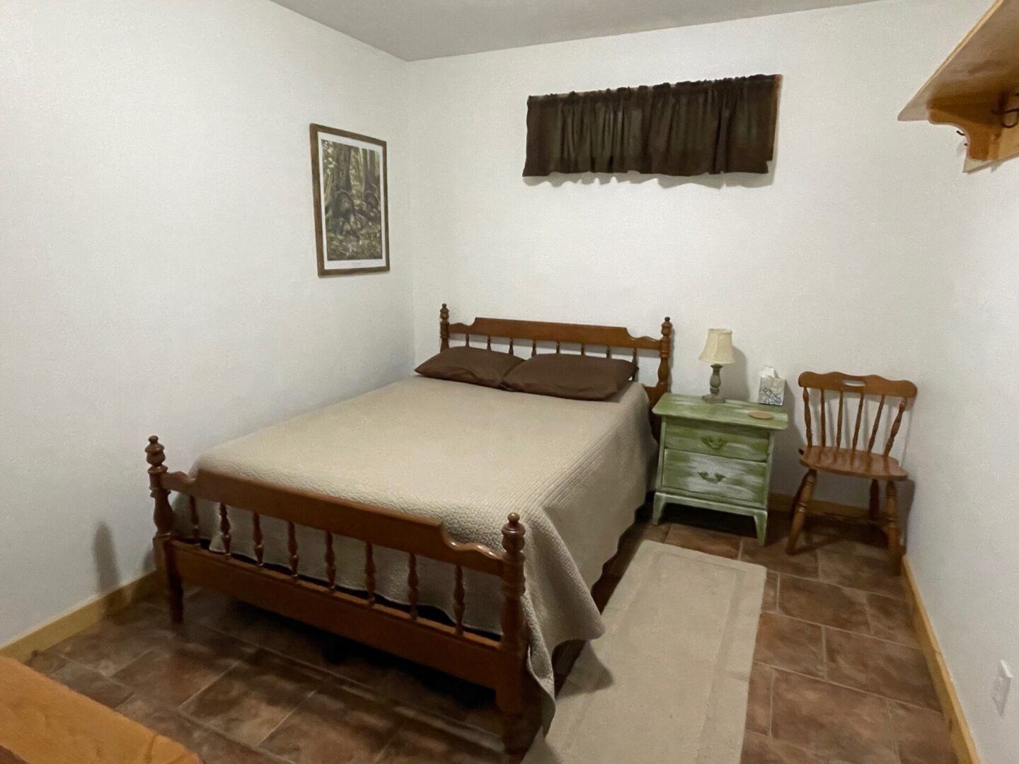 Small bedroom with a bed, nightstand, chair, and framed wall art on white walls and wood flooring