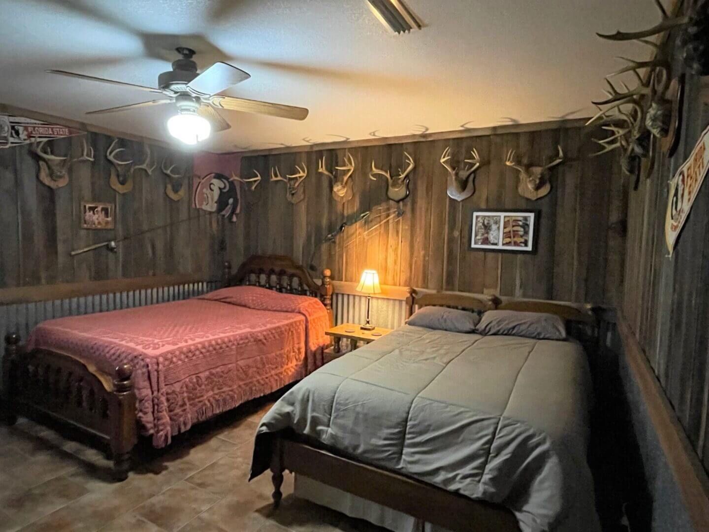 Rustic bedroom with two beds, antler decor, and a warm lamp by the wall.