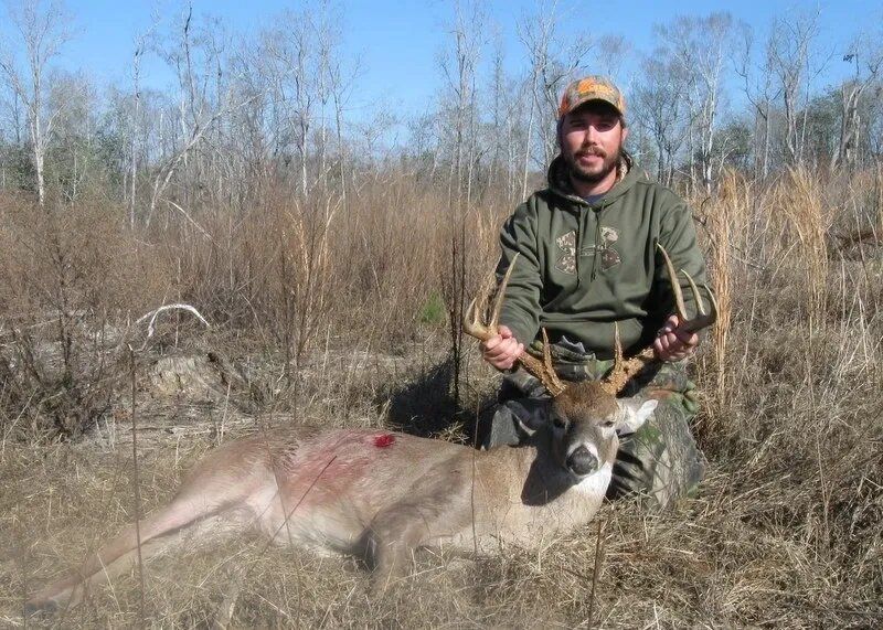 Hunter kneeling beside a deer in a dry field, holding the antlers under a clear sky