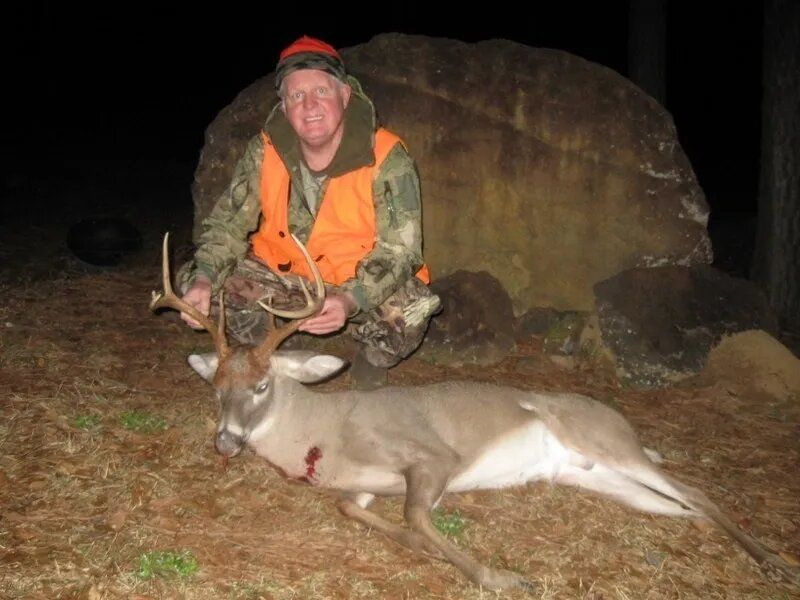 Hunter kneels behind a large deer with antlers at night beside a rock