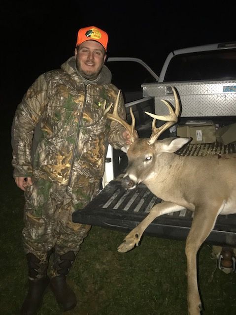 Hunter in camo standing beside a deer on a truck tailgate at night.