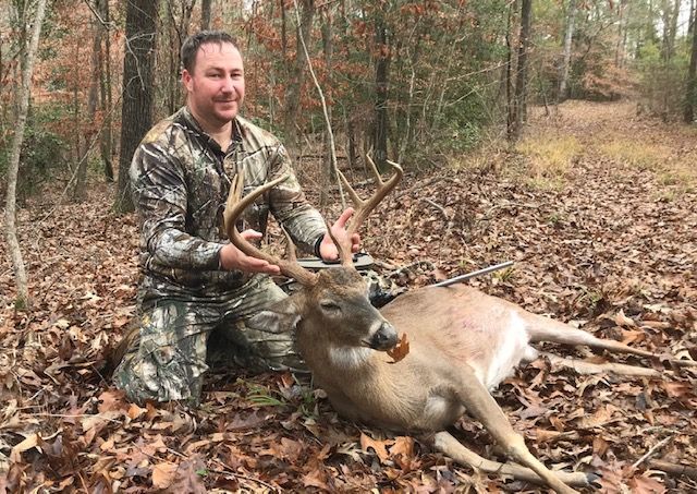 Hunter kneeling beside a deer in a leaf-covered forest