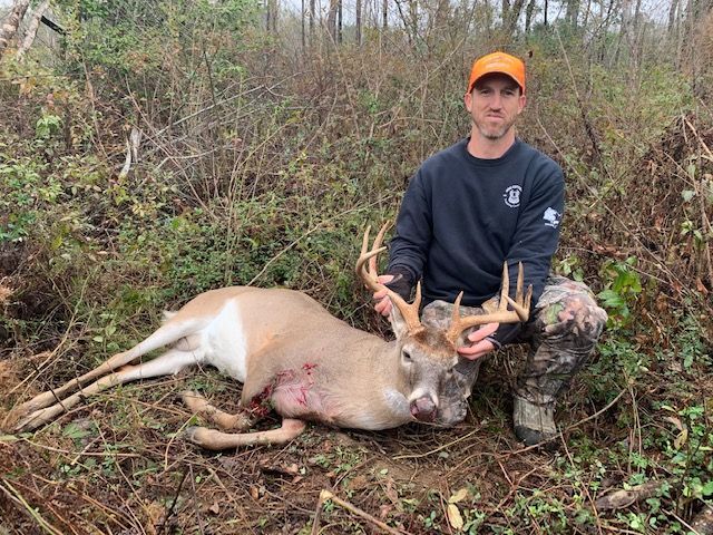 Hunter kneeling beside a deer he has just harvested in a wooded area