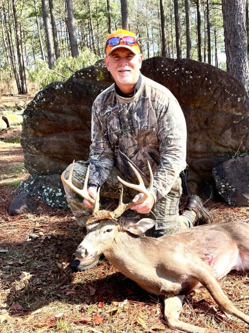 Hunter kneeling beside a deer he has just harvested in a wooded area.
