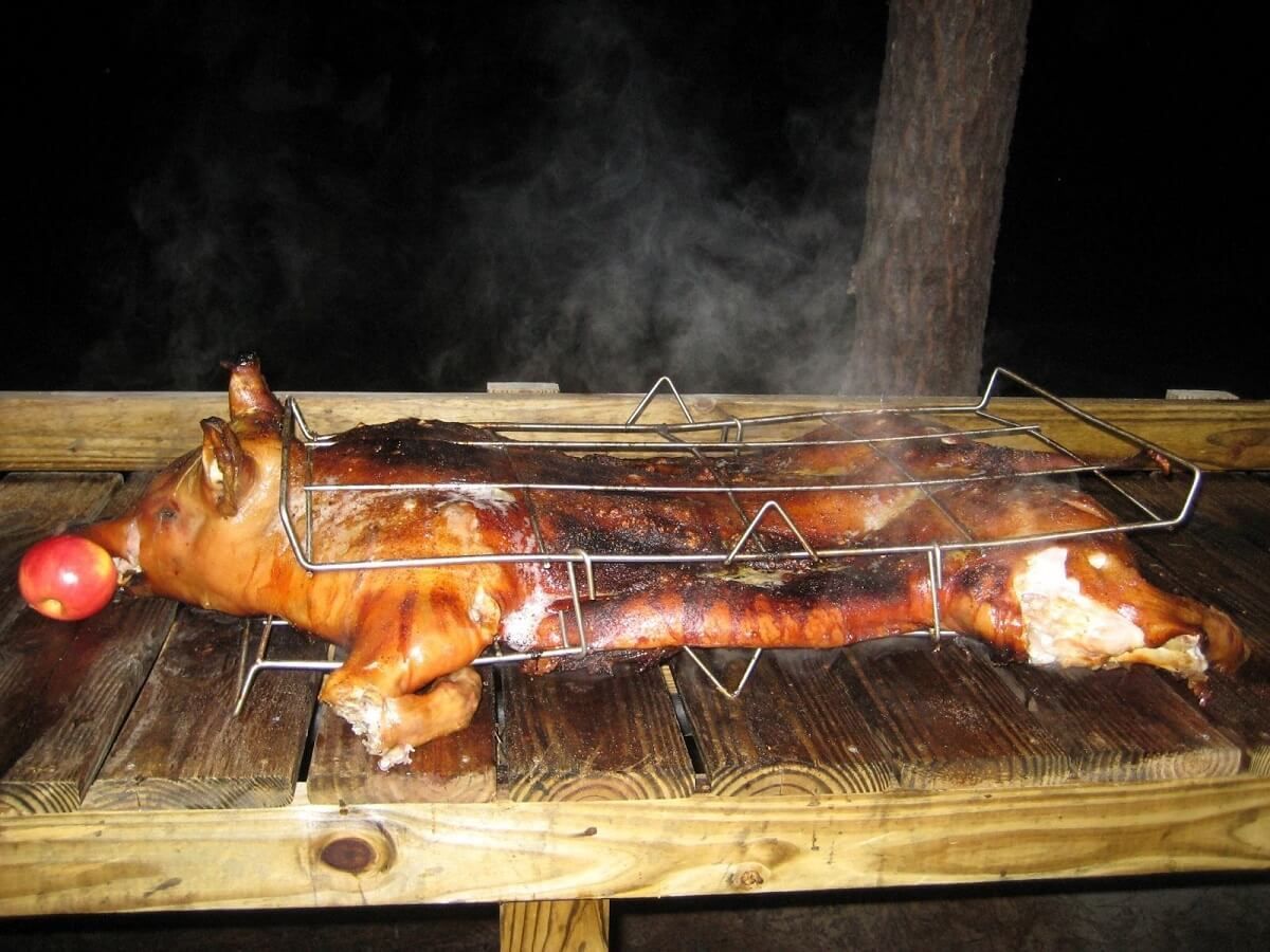 Whole roasted pig on a wooden table, steaming and held on a metal rack.