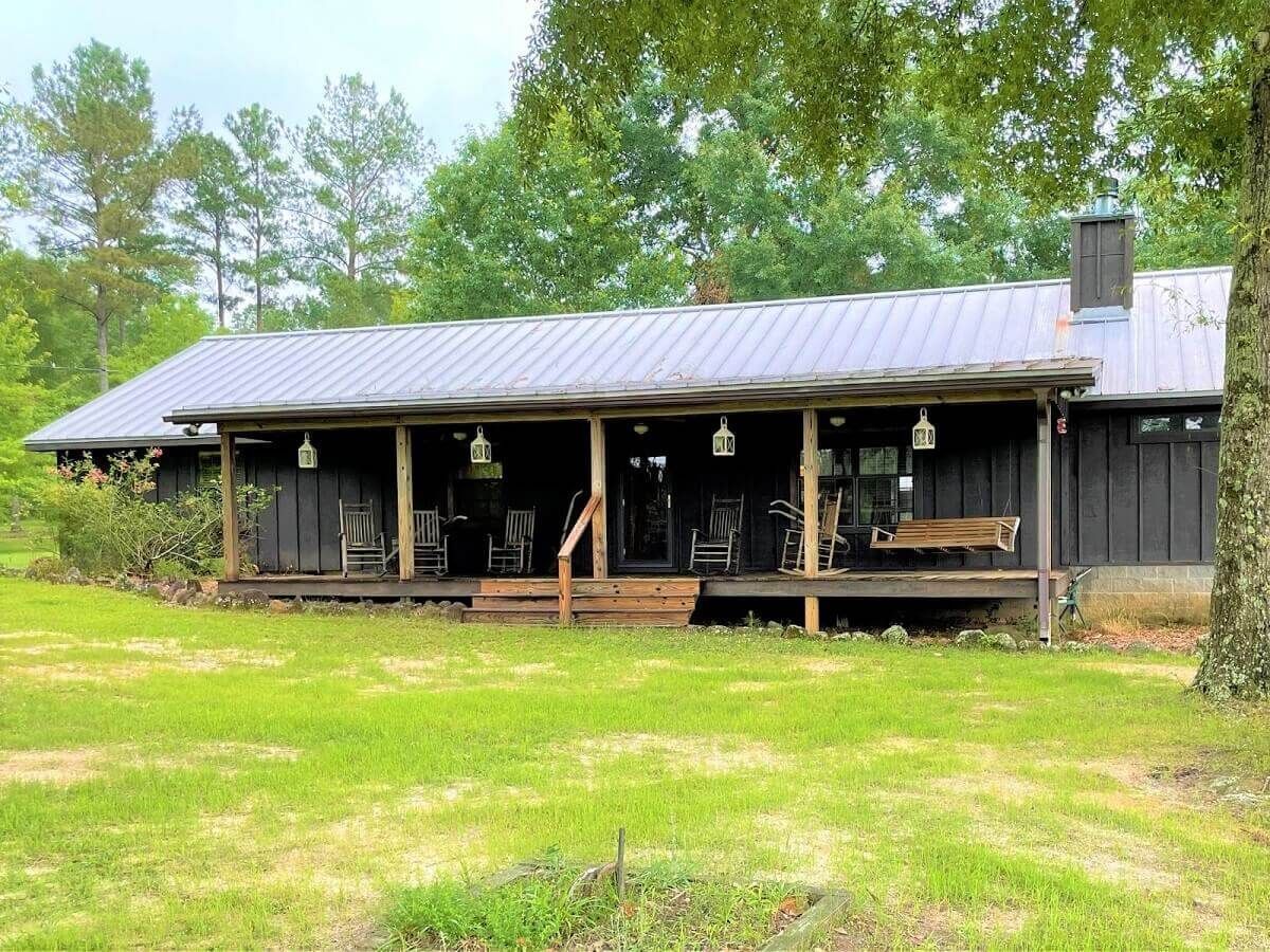 Rustic cabin with a metal roof and porch in a grassy clearing surrounded by trees.
