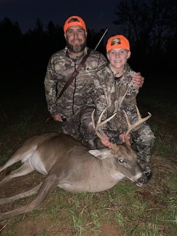 Two hunters in camo pose at night with a deer they’ve just harvested.