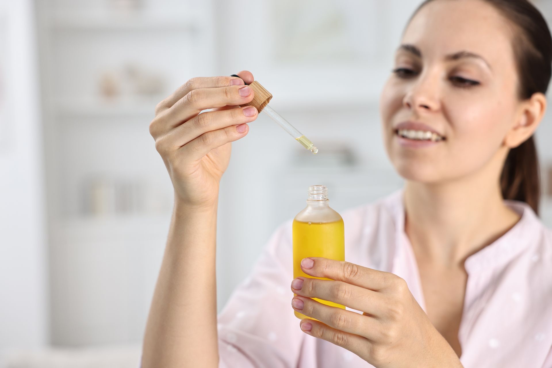 Eine Frau hält in einem hellen Badezimmer eine Pipette über eine gelbe Serumflasche.