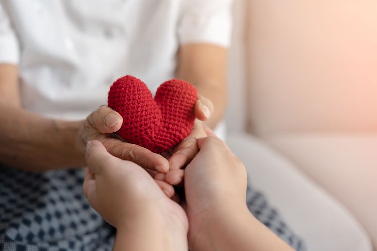Hände halten ein rotes Strickherz in einer gemütlichen Inneneinrichtung