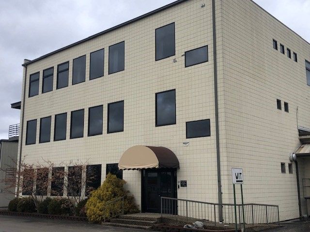 Two-story building with beige tiled facade, dark windows, and awning over the entrance.