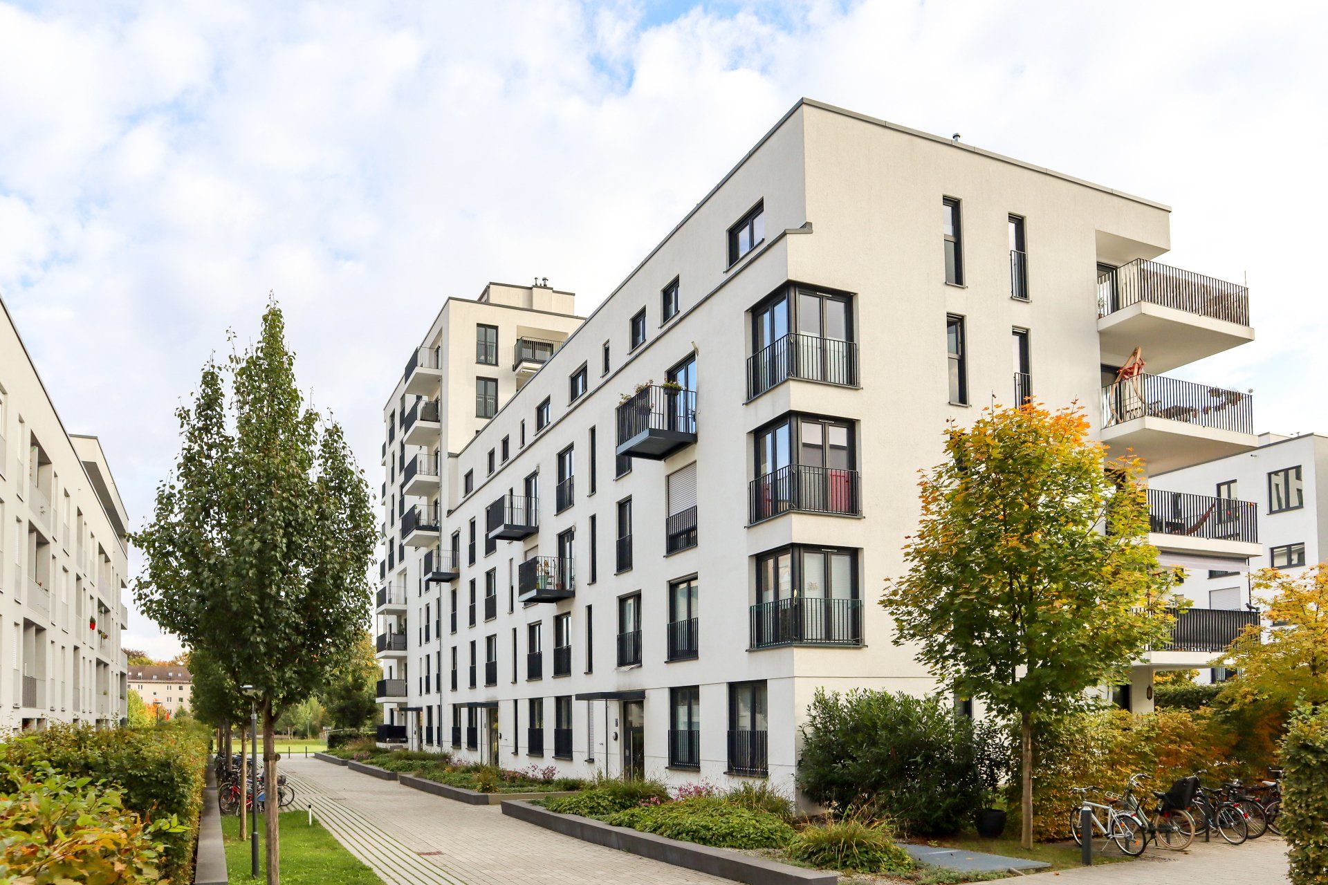 A large apartment building with a lot of windows is surrounded by trees and a sidewalk.