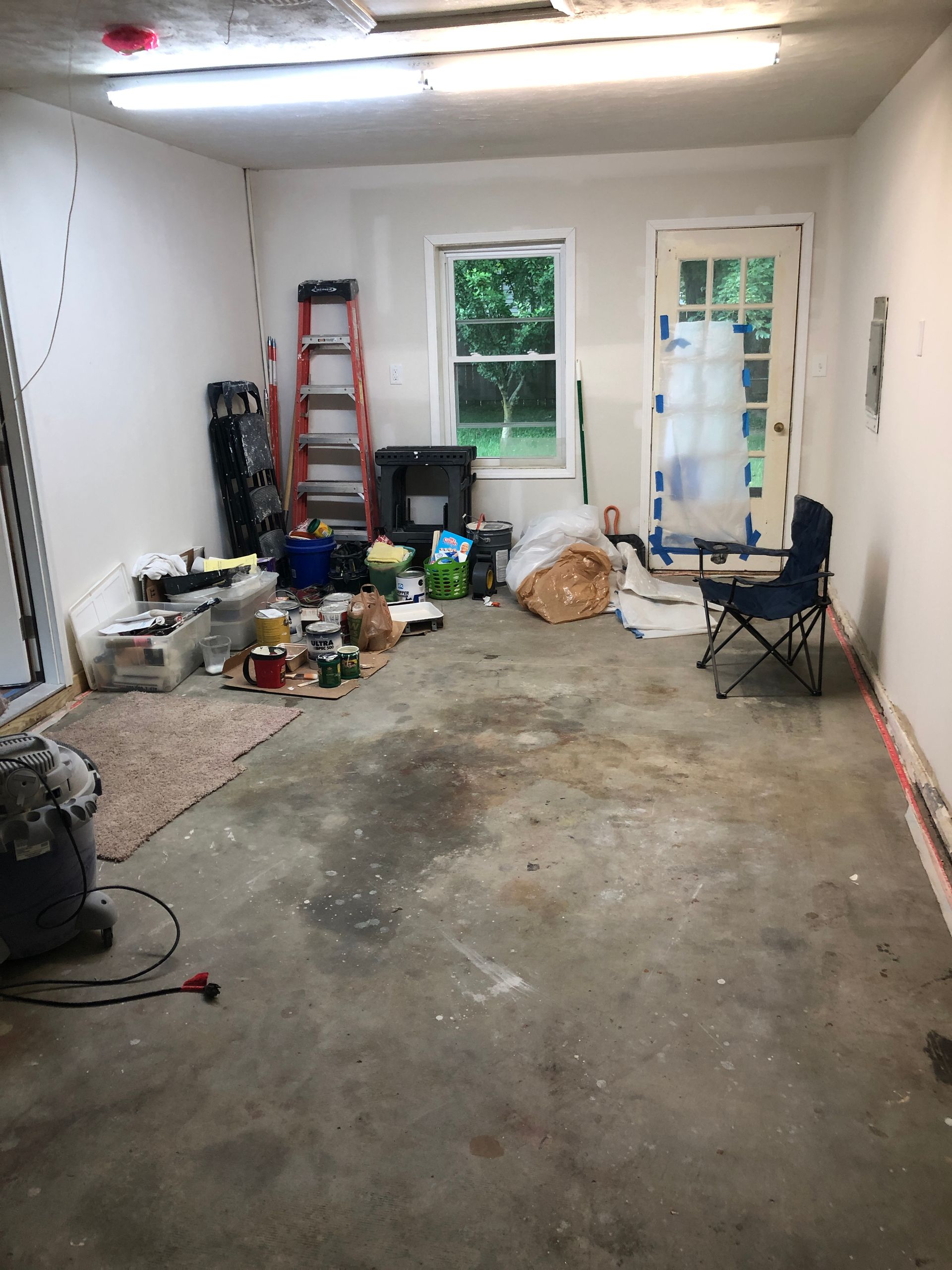 Cluttered garage or workshop with tools, ladder, chairs, and debris on a concrete floor