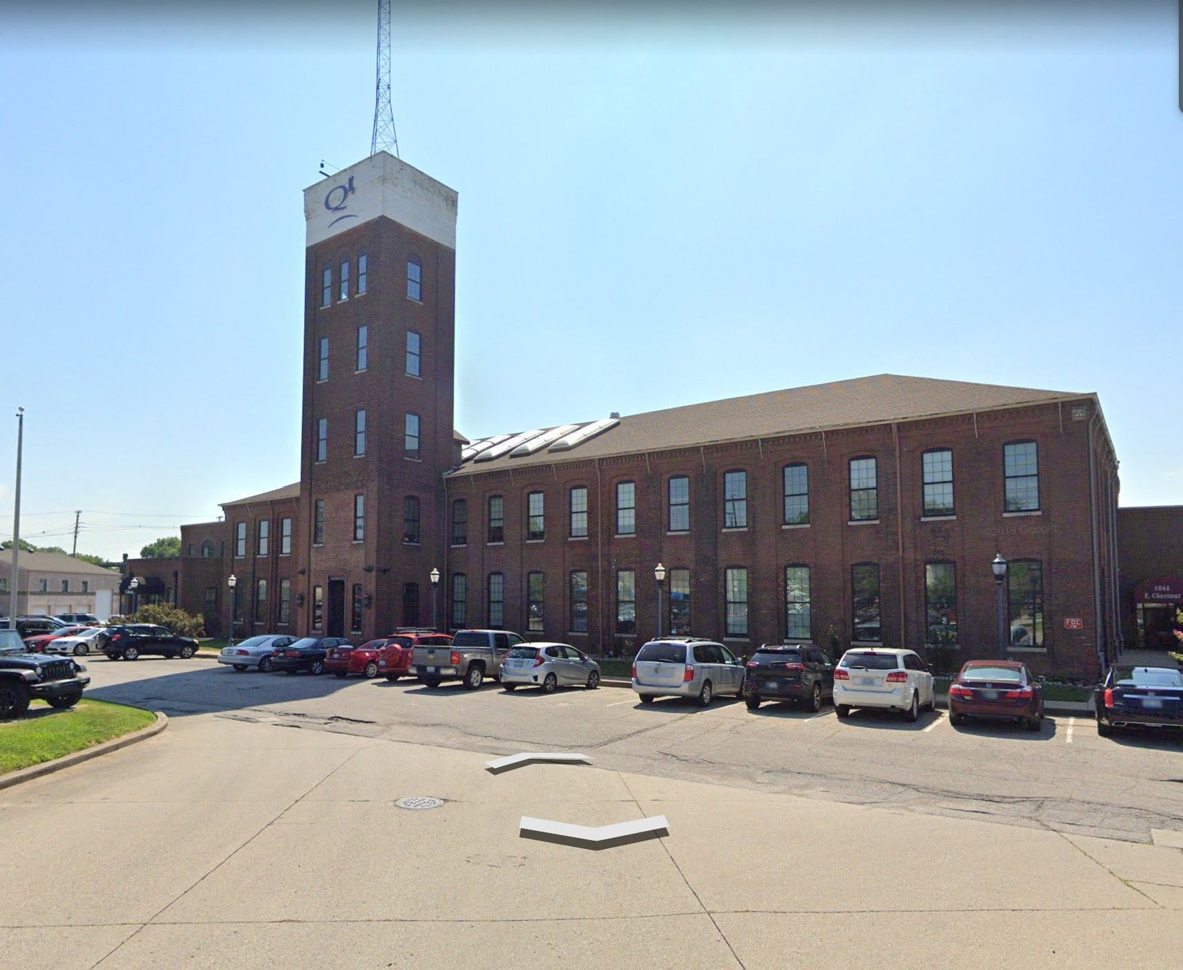 Brick building with tall tower and parking lot full of cars.