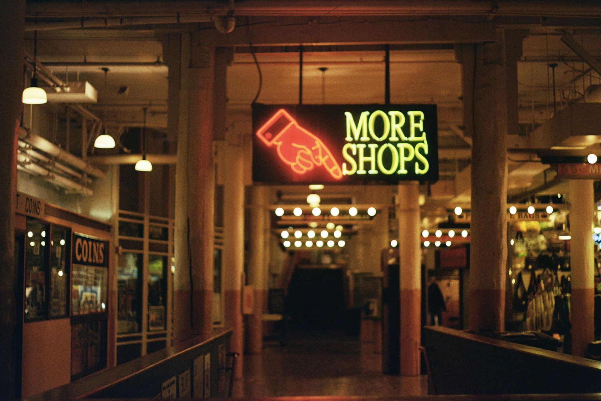 Neon “MORE SHOPS” sign above a dimly lit shopping arcade entrance