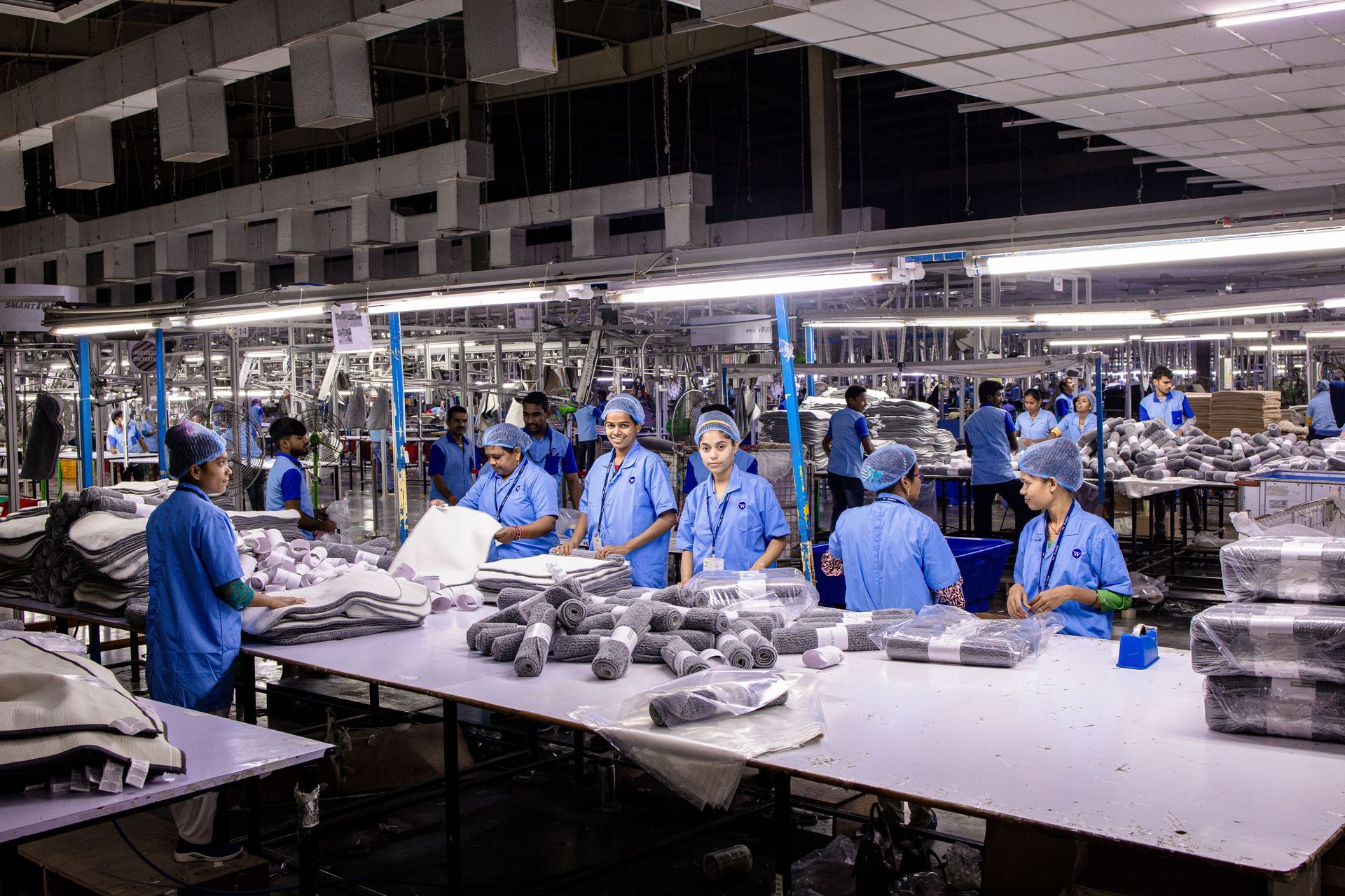 Workers in blue uniforms assembling products on a factory line under bright lights