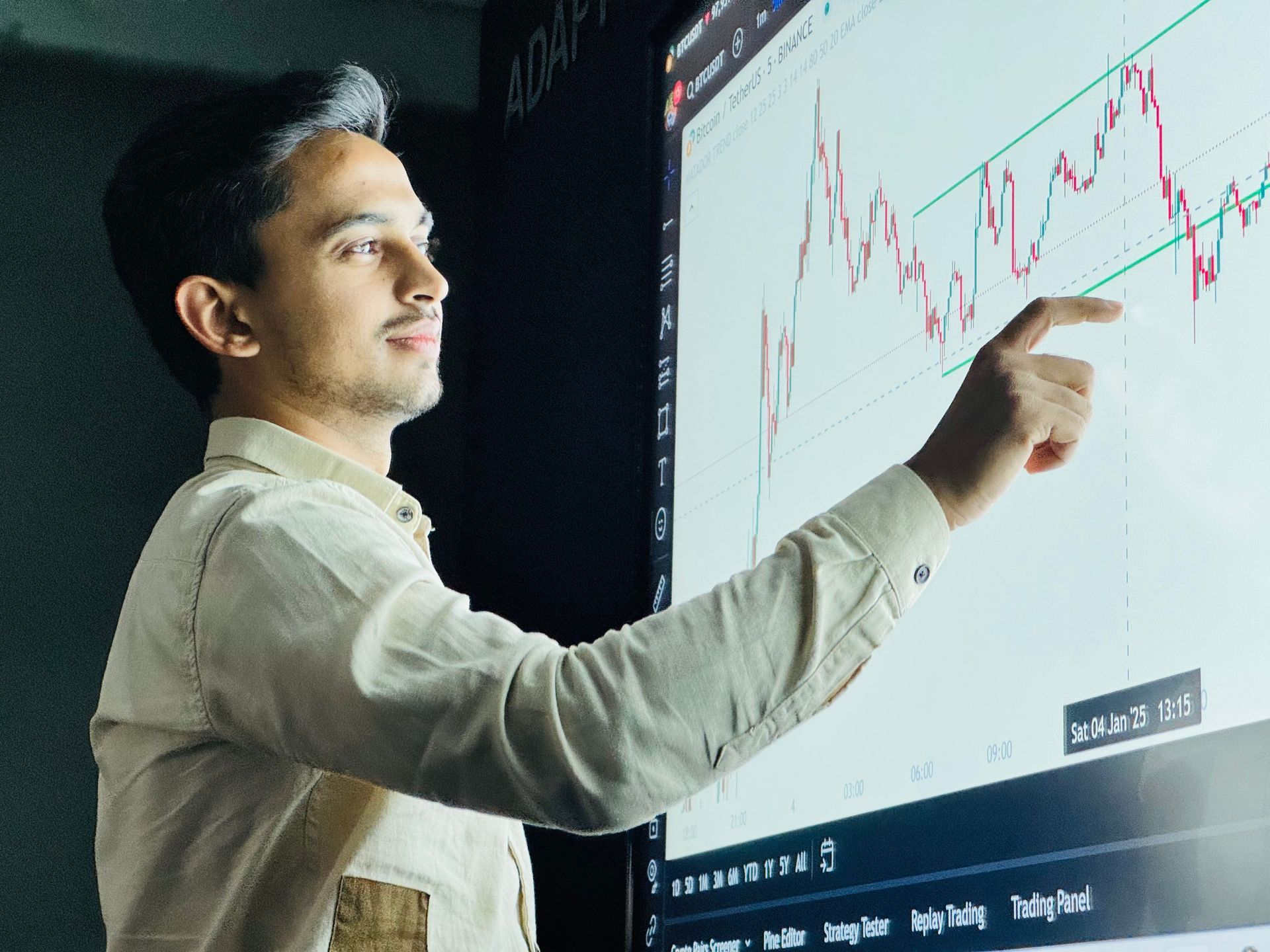 Person pointing at a stock chart on a large screen in a dark room