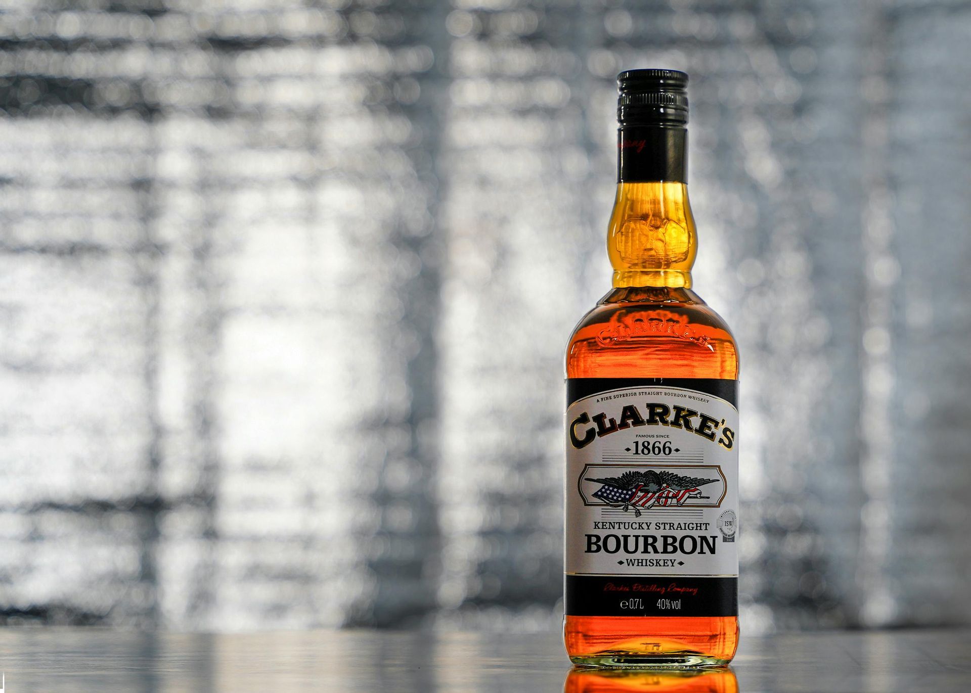 Bottle of Clarke's Bourbon whiskey against a blurred silver background.