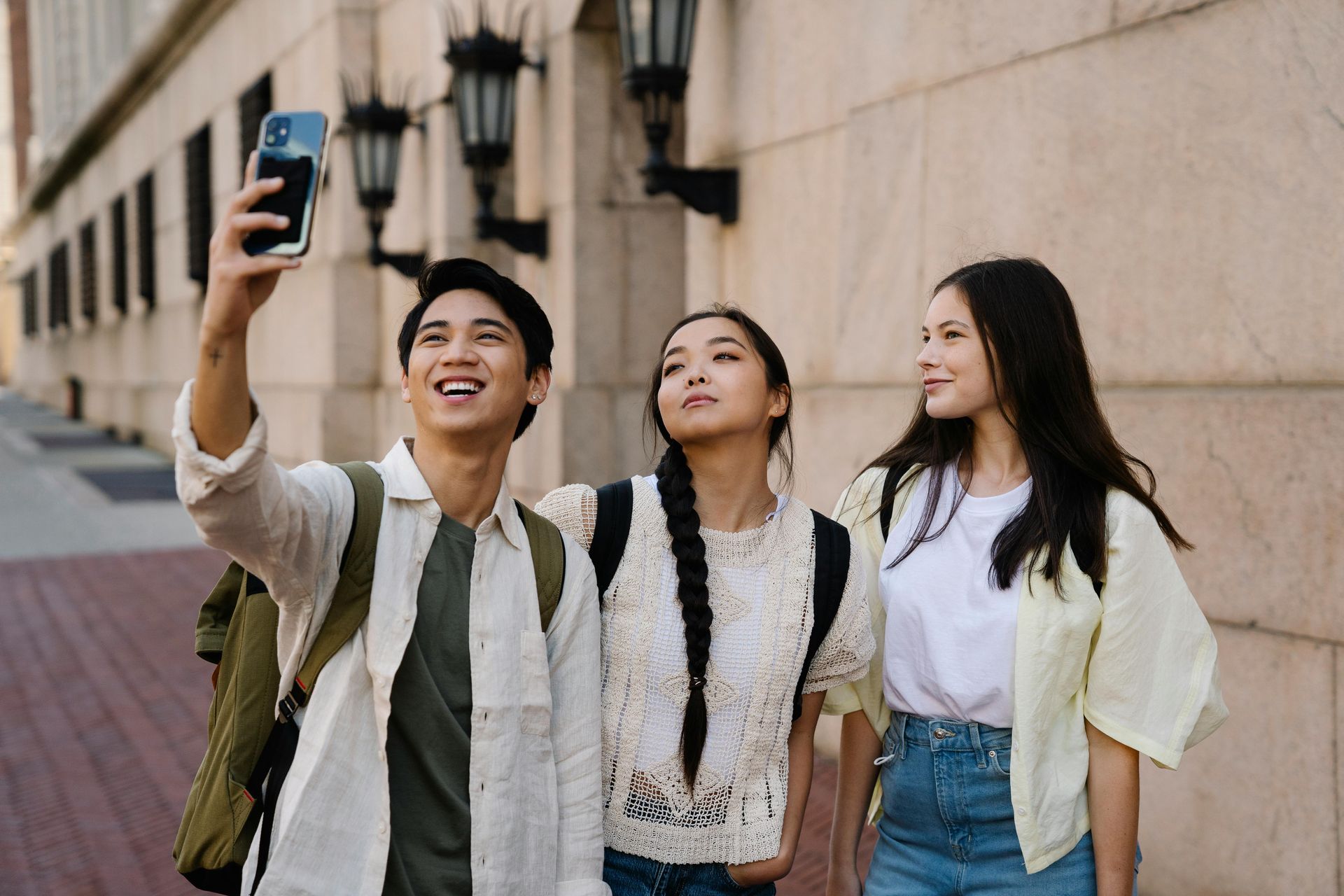 Three friends taking a selfie on a sidewalk beside a stone building