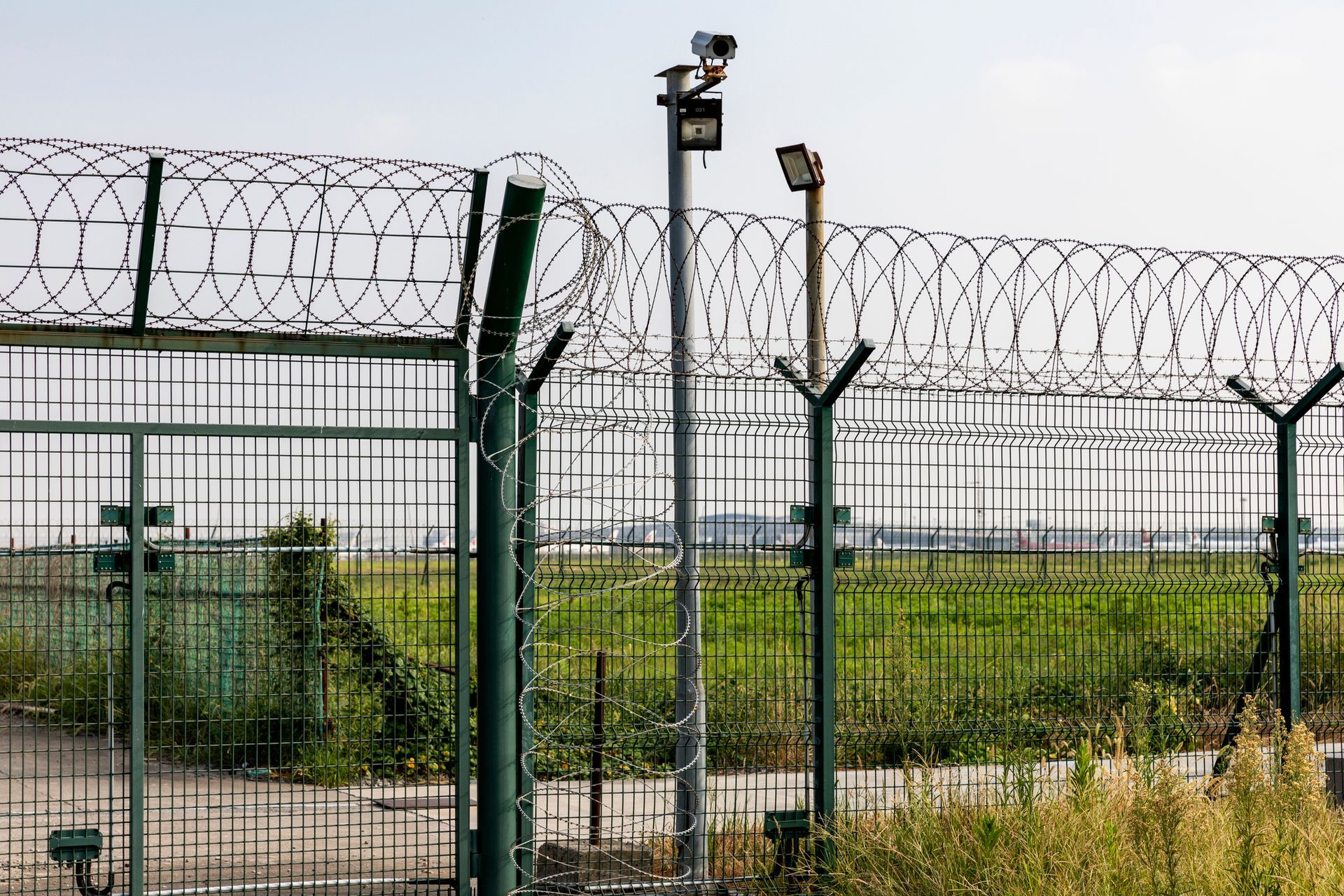 Security fence with razor wire, surveillance cameras, and field. Security fence with razor wire, surveillance cameras, and field.