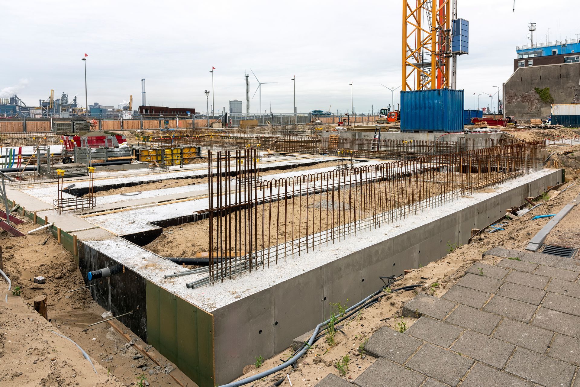 Construction site with concrete foundation, rebar, and crane in a coastal area. Construction site with concrete foundation, rebar, and crane in a coastal area.