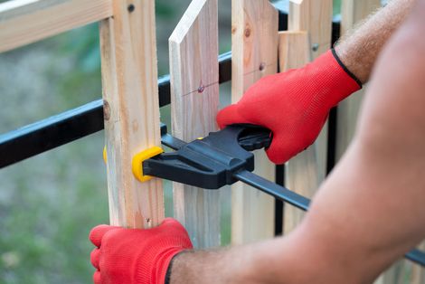 Hands in red gloves using a clamp to secure wooden fence slats. Hands in red gloves using a clamp to secure wooden fence slats.