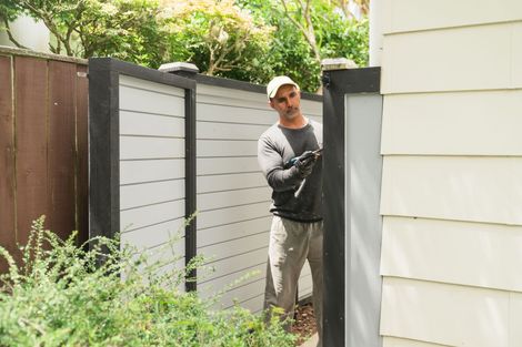Man painting fence with black trim, wearing work clothes, outside, near house. Man painting fence with black trim, wearing work clothes, outside, near house.