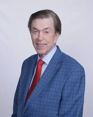 Portrait of a smiling man in a blue blazer and red tie against a light background